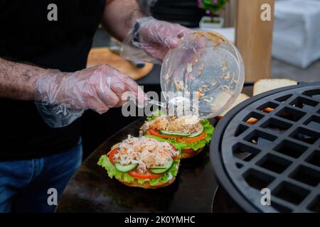 Küchenchef bereitet Burger mit Meeresfrüchten zu, Fisch auf dem Brazier auf dem Sommer-Lebensmittelmarkt Stockfoto