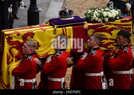 Die Trägerpartei der Queen's Company, 1. Bataillon Grenadier Guards, trägt den Sarg von Königin Elizabeth II., der im Royal Standard mit der oben platzierten Kaiserlichen Staatskrone drapiert ist, in die Westminster Hall, London, wo er vor ihrer Beerdigung am Montag im Zustand liegen wird. Bilddatum: Mittwoch, 14. September 2022. Stockfoto