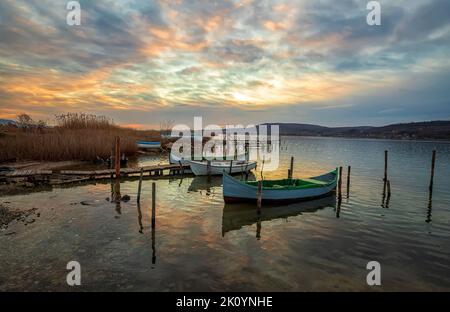 Der ruhige Nachmittag auf einem See mit einem hölzernen Pier und Booten am bunten Himmel. Stockfoto