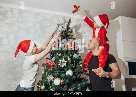 Familie - Mama, Papa und Sohn schmücken den Weihnachtsbaum von oben in ihrer Wohnung. Stockfoto