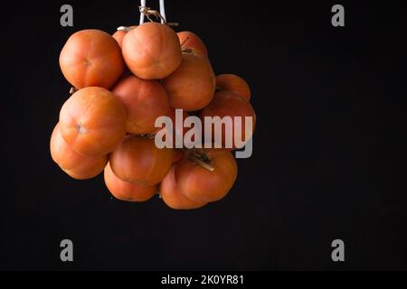 Eine zum Trocknen hängende Kirschtomate isoliert auf einem schwarzen Hintergrund Stockfoto