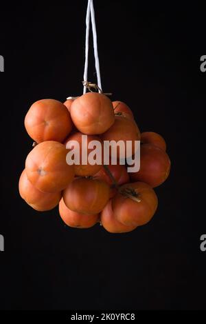 Eine zum Trocknen hängende Kirschtomate isoliert auf einem schwarzen Hintergrund Stockfoto