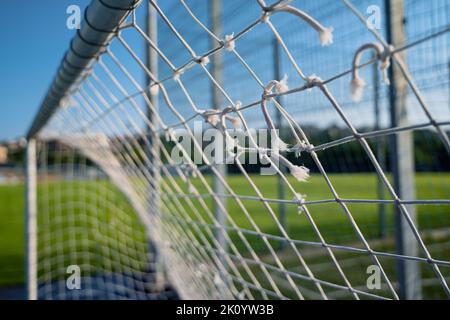 Nahaufnahme von beschädigten Fußball-Tor-Torpfosten weißes Seilnetz mit Knoten und grünem Feld und blauem Himmel im Hintergrund Stockfoto