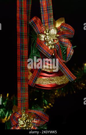 Weihnachtsglocken mit roter Schleife und goldenem Engel auf schwarzem Hintergrund. Stockfoto