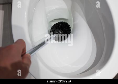 Die Hand reinigt eine weiße Toilettenschüssel mit einer Bürste. Hausarbeit. Draufsicht. Nahaufnahme. Stockfoto