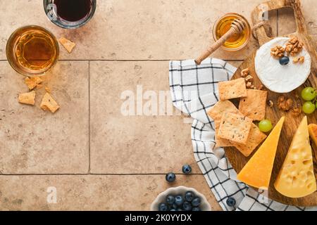 Auswahl an Käse, Honig, Cracker, Heidelbeeren, Trauben mit Rot-und Weißwein in Gläsern Antipasto Server auf weißem Marmorbrett auf grauem Hintergrund Stockfoto