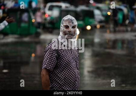 Dhaka, Bangladesch. 14. September 2022. Ein Mann posiert wegen eines Fotos, der seinen Kopf wegen Regen mit einer Plastiktüte bedeckt, während er am Mittwoch, 14. September 2022, nach Hause nach dem Büro in Dhaka, Bangladesch, geht. Die Hauptstadt Dhaka verzeichnete in den letzten 24 Stunden unter dem Einfluss des Niederdrucks in der Bucht von Bengalen 53 mm Regen. (Bild: © Md. Rakibul Hasan/ZUMA Press Wire) Bild: ZUMA Press, Inc./Alamy Live News Stockfoto