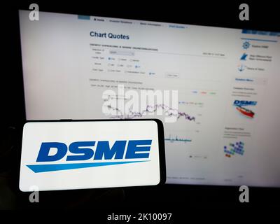 Person mit Mobiltelefon und Logo von Daewoo Shipbuilding and Marine Engineering (DSME) auf dem Bildschirm vor der Webseite. Konzentrieren Sie sich auf die Telefonanzeige. Stockfoto