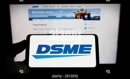 Person, die das Smartphone mit dem Logo von Daewoo Shipbuilding and Marine Engineering (DSME) auf dem Bildschirm vor der Website hält. Konzentrieren Sie sich auf die Telefonanzeige. Stockfoto