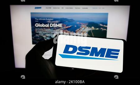 Person mit Mobiltelefon und Logo von Daewoo Shipbuilding and Marine Engineering (DSME) auf dem Bildschirm vor der Webseite. Konzentrieren Sie sich auf die Telefonanzeige. Stockfoto