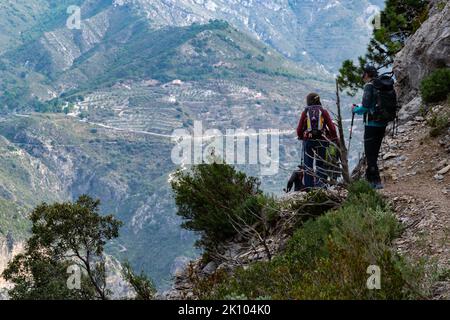 Wanderer gehen einen Pfad in der Sierra de Tejeda und Almijara mit einer Bergmauer im Hintergrund hinunter Stockfoto