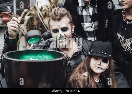 Beängstigende Familie, Mutter, Vater, Töchter, die Halloween feiern. Kessel des Trank. Erschreckende schwarze Schädel Halbgesicht Make-up, Hexe Kostüme, stilvolle Bild Stockfoto