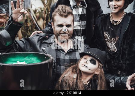 Beängstigende Familie, Mutter, Vater, Töchter, die Halloween feiern. Kessel des Trank. Erschreckende schwarze Schädel Halbgesicht Make-up, Hexe Kostüme, stilvolle Bild Stockfoto