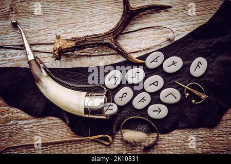 Oben Ansicht von Runensteinen mit verschiedenen objekten aus der wikingerzeit, Trinkhorn, Bronzebrosche, Glasperlen auf Lederband. Uralte Weissagung. Stockfoto