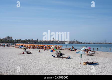 Blick auf den Strand Spiaggia del Lido di Alghero in der Nähe der Altstadt von Alghero, Sardinien, Italien mit der Altstadt und dem Hafen im Hintergrund Stockfoto