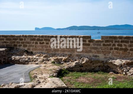 Blick über die Mauer der Stadtmauer der Altstadt von Alghero, Sardinien, Italien mit den Klippen von Capo Caccia und dem Vorgebirge in der Ferne Stockfoto