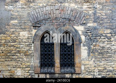 Zwei Bogenfenster mit Metallstangen an der alten Festungsmauer aus grauem und beigem Stein. Aus der „Window of the World“-Serie. Stockfoto