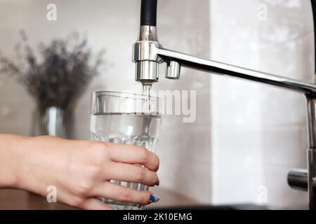 Frau, die in der Küche Trinkglas mit Leitungswasser füllte. Konzept für sauberes Trinkwasser zu Hause. Frisches Getränk gießen. Wasserqualitätsprüfung Konz Stockfoto
