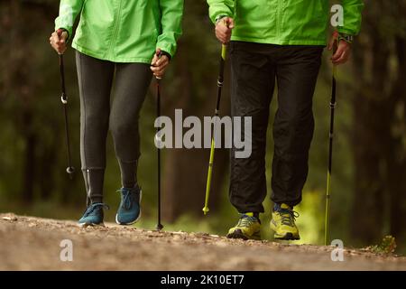 Beschnittenes Bild von Frau und Mann, die mit skandinavischen Stöcken im Herbstwald im Freien spazieren. Nordic Walking, gesunder Lebensstil Stockfoto