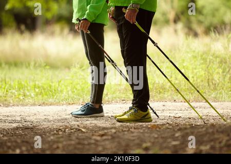 Beschnittenes Bild von Frau und Mann, die mit skandinavischen Stöcken im Herbstwald im Freien spazieren. Nordic Walking, gesunder Lebensstil Stockfoto