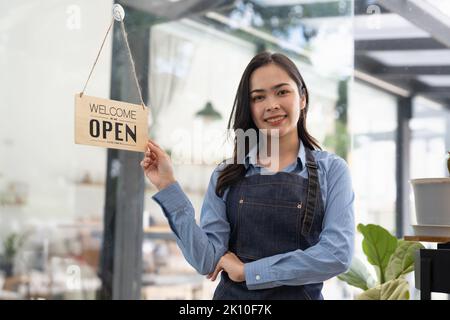 Junge Asienmanagerin, die ein Schild vom geschlossenen zum offenen Schild am Türcafé änderte und nach der Absperrung auf Gäste wartete. Besitzer kleines Unternehmen Stockfoto