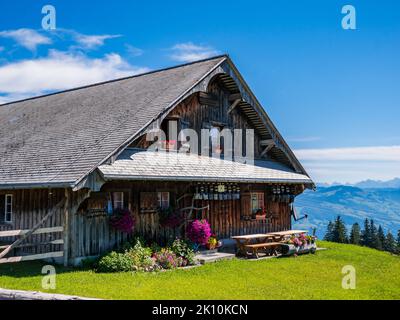 Ein schönes Holzhaus auf einer Bergwiese in der Schweiz mit Blumen in den Fenstern Stockfoto