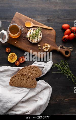 Der Camembert-Käse ist rund, gegrillt, mit goldenem Honig auf einem hölzernen Schneidebrett gegossen. Weicher selektiver Fokus, schwarzer Hintergrund.Platz zum Kopieren. Gesunde Ernährung. Vertikales Foto. Stockfoto