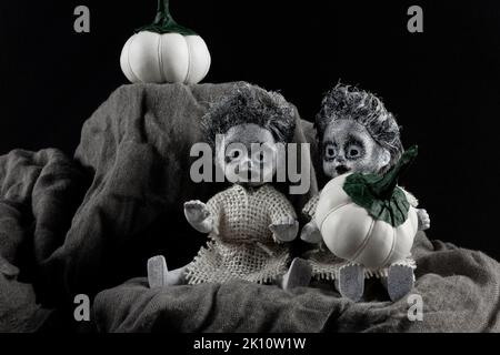 Frohe Halloween-Feiertage. Zwei gruselige Zombie Puppen mit weißen Kürbissen auf dunklem Hintergrund. Stockfoto