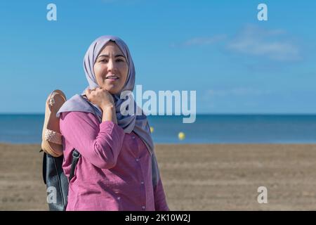 Muslimische Frau am Strand, die auf die Kamera schaut Stockfoto