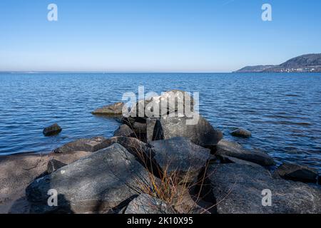 Felsbrocken als Teil eines Wellenbrechers in einem See. Bild vom See Vattern, Schweden. Blaues Wasser und Himmel im Hintergrund Stockfoto