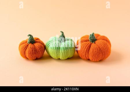 Gestrickte orangefarbene und grüne Kürbisse auf orangefarbenem Hintergrund, Herbstkomposition, Vorderansicht. Halloween-Konzept. Stockfoto