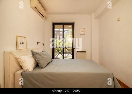 Schlafzimmer mit Doppelbett mit Kopfteil mit grauen Kissen, brauner Aluminiumbalkon mit Blick auf den Garten Stockfoto