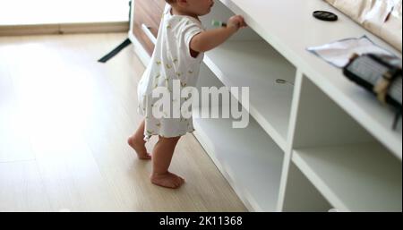 Baby steht auf Möbeln zu Hause Wohnzimmer lehnt. Kleinkind berühren Objekt, Kleinkind Junge mit der Hand greifen Stockfoto