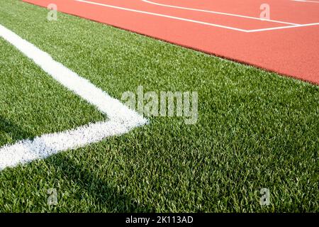 Hintergrund des Sportstadions. Rote Kunstkautschuk-Platz Boden und weiße Linie und grünen Kunstrasen Fußballplatz Stockfoto