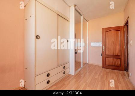 Schlafzimmer mit schäbigen weißen Holzschrank mit zwei Türen und einem weiteren Einbauschrank mit Spiegelschiebetüren Stockfoto