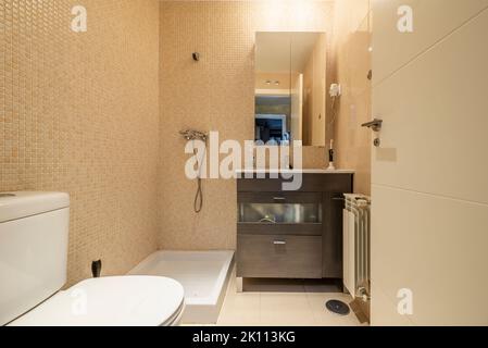Badezimmer mit rahmenlosem Spiegel, Waschbecken mit dunklem Holzschrank und weißer Holztür Stockfoto