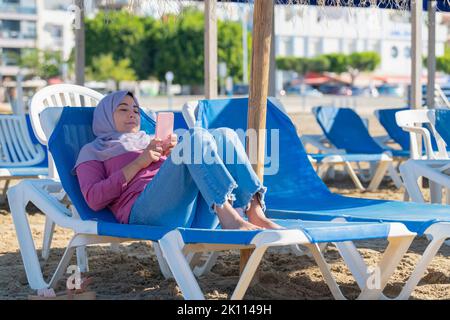Eine arabische Frau auf einer Sonnenliege, die ihr Telefon überprüft Stockfoto
