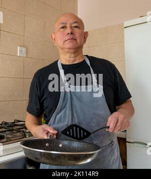 Portrait eines älteren Mannes, Koch, der in der Küche eine Mahlzeit zubereitet. Stockfoto