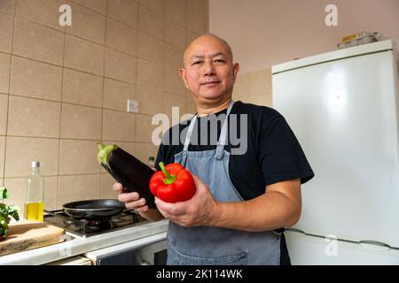 Portrait eines älteren Mannes, Koch, der in der Küche eine Mahlzeit zubereitet. Stockfoto
