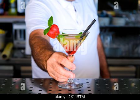 Barkeeper serviert an sonnigen Tagen frischen gelben, roten Sommerobstcocktail an der Theke. Ausgewählter Fokus, geringe Schärfentiefe. Stockfoto