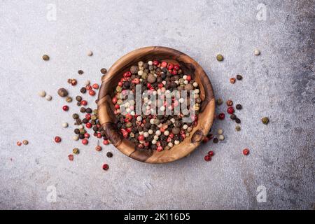 Draufsicht auf Mix-Pfefferkörner in Holzschüssel für würzige und aromatische Speisen auf grauem Beton-Hintergrund Stockfoto