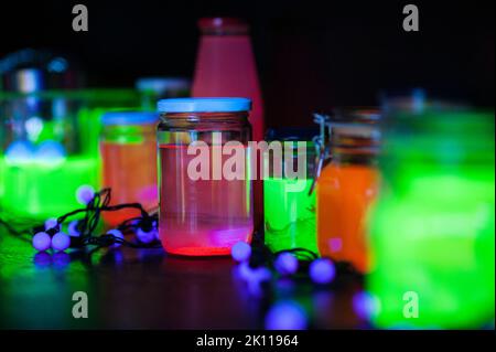 Glasgläser mit neongrüner, orangefarbener und pinker Flüssigkeit auf einem Regal auf einer lustigen, coolen Halloween-Party im Innenbereich. Hippe, festliche und kreative Dekorationsideen. Stockfoto