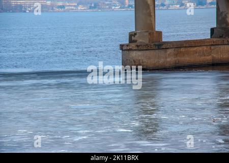 Im Frühjahr driftet eine dünne Eisscholle stromabwärts und schwimmt an der Brückenstütze vorbei. Stockfoto