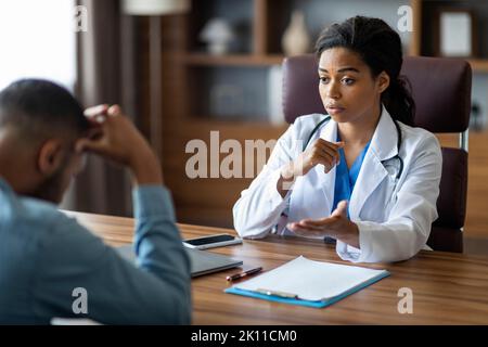 Schwarze Frau Arzt mit Gespräch mit verärgert kranken Mann Patient Stockfoto