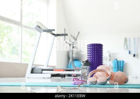 Schaumstoffrolle mit Kopfhörern, Hanteln, Flasche und Springseil auf Matte im Fitnessstudio Stockfoto