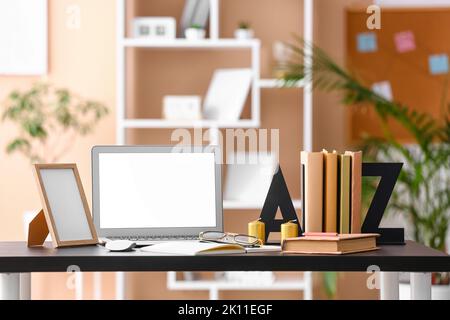 Arbeitsplatz mit Laptop, Halter, Büchern, Rahmen und Kerzen im Zimmer Stockfoto