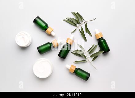 Flaschen mit ätherischem Olivenöl und Gläser mit Creme auf weißem Hintergrund Stockfoto