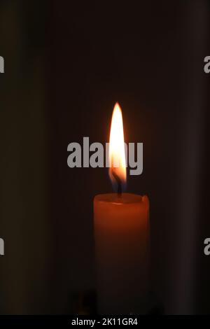 Unschärfe-Nahaufnahme von Kerzenlicht und Flamme auf schwarzem Hintergrund. Vertikal. ZERREISST die Flamme. Speicher. Nicht fokussiert. Stockfoto