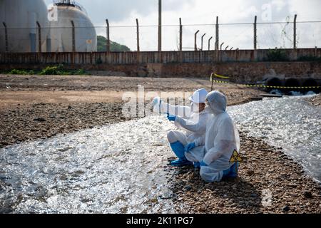 Ökologe Probenahme Wasser giftige Chemikalien aus dem Fluss mit Reagenzglas und haben weißen Rauch, Biologe tragen Schutzanzug und Maske sammelt Probe Stockfoto
