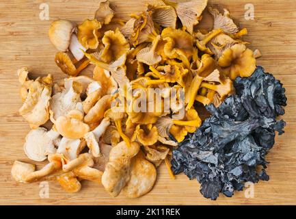 Ernte von verschiedenen essbaren Wildpilzen (Gelbfuß, blaue Pfifferlinge, Igel) auf einem Holzschneidebrett. Stockfoto